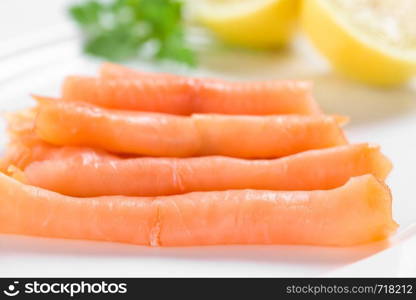 Smoked salmon slices with lemon halves on white plate (Selective Focus, Focus on the front of the first slice) . Smoked Salmon Slices