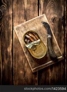 Smoked sprats in oil with an old tin with a knife. On wooden background.. Smoked sprats in oil