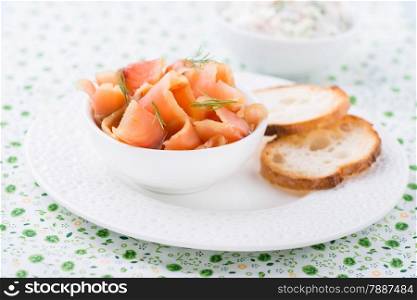 Smoked wild salmon and baguette on white plate, selective focus