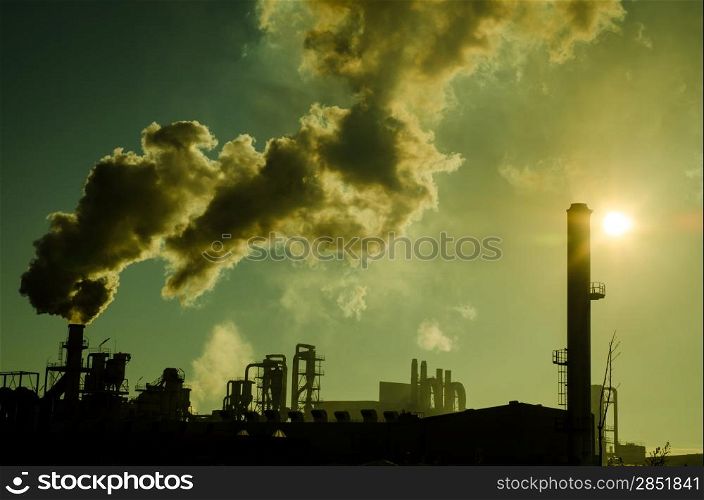 Smoking chimney at sunset on industrial buildings complex.