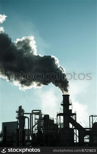 Smoking chimney at sunset on industrial buildings complex.