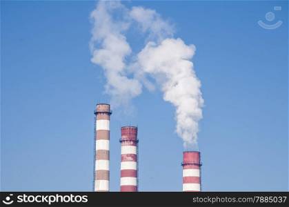 Smoking chimneys of thermal power plant on clear blue sky background
