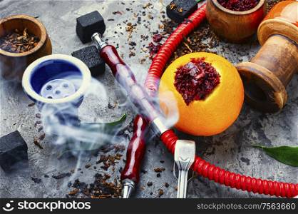 Smoking hookah pipe with mouthpiece and citrus flavored shisha tobacco.. Oriental hookah with orange flavor.