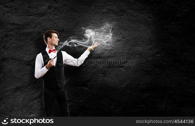 Smoking pipe. Young handsome businessman smoking pipe against black background