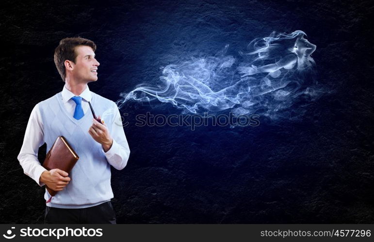 Smoking pipe. Young handsome businessman smoking pipe against black background