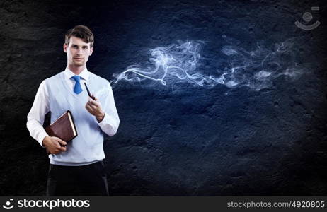 Smoking pipe. Young handsome businessman smoking pipe against black background