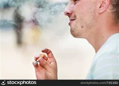 Smoking problem, addiction to nicotine concept. Adult man in white shirt smoking cigarette outside.. Adult man smoking cigarette outside