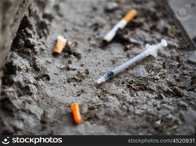 smoking, substance abuse, addiction and drug use concept - close up of syringe and smoked cigarette on ground