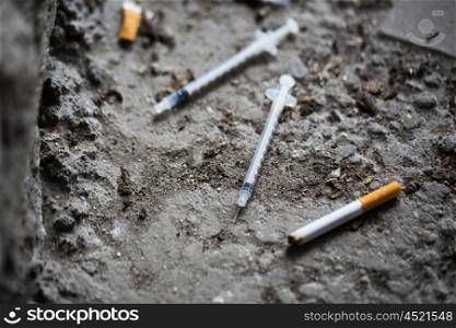 smoking, substance abuse, addiction and drug use concept - close up of syringe and smoked cigarette on ground