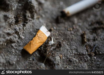 smoking, substance abuse, addiction, people and bad habits concept - close up of smoked cigarette butt on ground