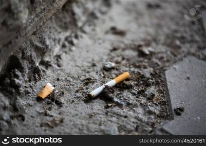 smoking, substance abuse, addiction, people and bad habits concept - close up of smoked cigarette butt on ground