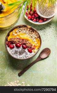 Smoothie bowl with mango and tropical fruits , chia seeds yogurt pudding and cranberries, nuts, oatmeal topping in coconut shells with spoon, top view. Healthy clean breakfast food. Summer vegan diet