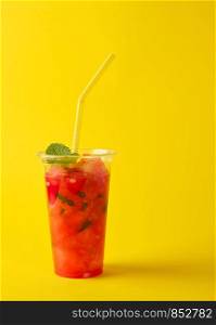 smoothie from ripe red watermelon in a plastic cup, close up, yellow background