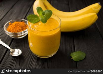 Smoothies with banana and turmeric on the black wooden background