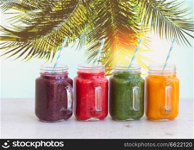Smoothy drinks in glass jars on white table under plam tree. Fresh smoothy drink