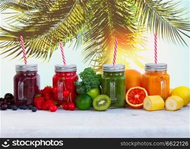 Smoothy drinks in glass jars with ingredients on white table under plam tree. Fresh smoothy drink