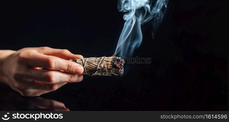 Smudging. Burning bundle of dried herb sage, black reflective background. Cleansing negative energy and purifying space.. Smudging with Smoke from Dried Sage Smudge Stick