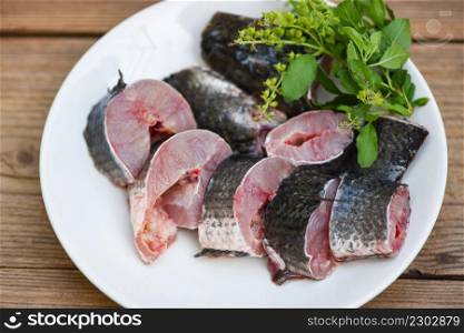 Snakehead fish for cooking food, striped snakehead fish chopped with ingredients holy basil leaf on white plate and wooden table kitchen background, Fresh raw Snake head fish menu freshwater fish