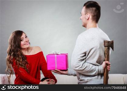 Sneaky insincere man holding axe giving gift present box to woman. Husband concealing hiding his true feelings from happy trusting wife. Untrue False intention. Relationship problems.