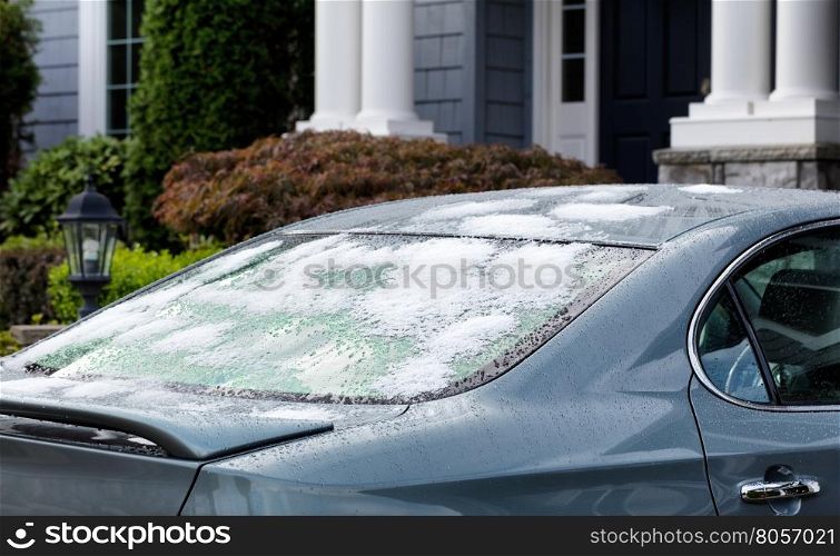 Snow and ice on back of car window. Cold weather concept for driving cars during winter. Selective focus on rear window of car with partial home in background.