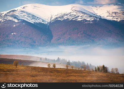 Snow caped mountain range. Morning fog in the valley. Spring and autumn misty scene. Misty hills
