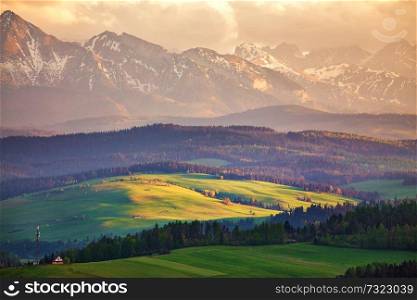 Snow caped mountains and green fields and meadows in Malopolska region, Poland. Spring sunset in Tatra Mountains, Pieniny range