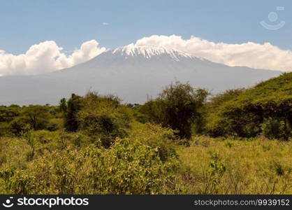 Snow capped Kenya’s Kilimanjaro mountain under cloudy blue sky captured on Kenya Africa safari.