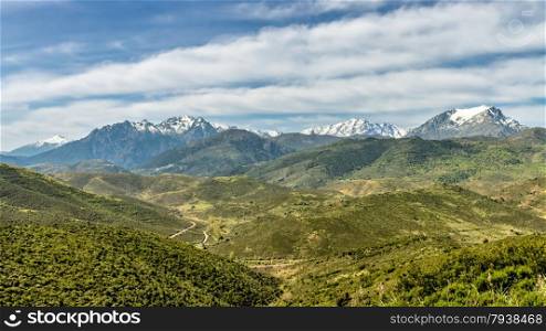 Snow capped Monte Padru and Asco mountains in Corsica with lush green maquis covered hills and valleys and tracks in the foreground