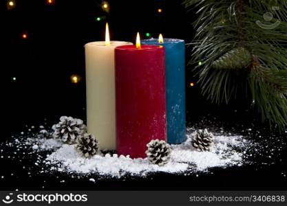 Snow cover candles and cones with fir and lights in background