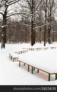 snow-covered benches in meadow of city park in winter