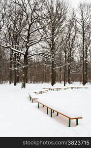 snow covered benches on glade of city park in winter