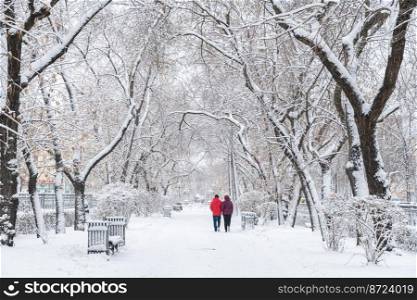 snow-covered city in winter. a man and a woman walk along a snowy alley.. snow-covered city. a man and a woman walk along a snowy alley