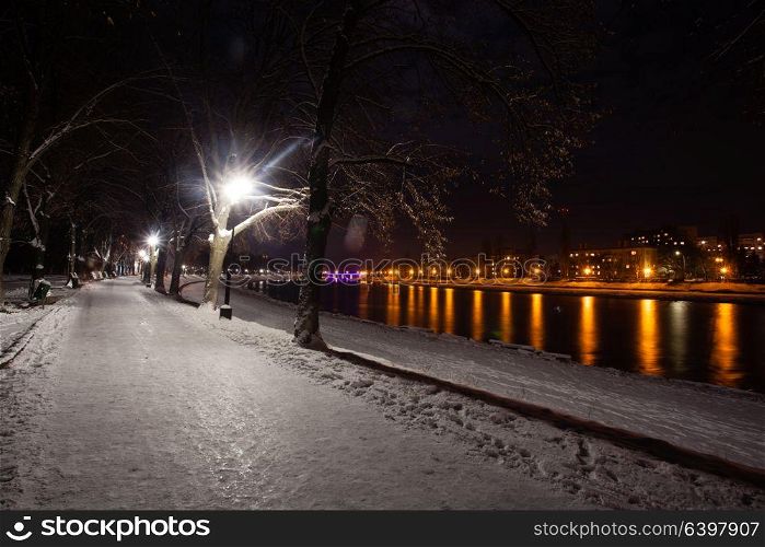 Snow-covered embankment in evening city. Beautiful winter landscape. Night view of snow-covered embankment