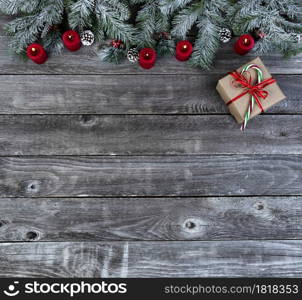 Snow covered evergreen branches with bright red burning candles and a giftbox, on faded wooden planks for a merry Christmas or happy New Year holiday celebration concept