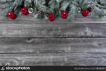 Snow covered evergreen branches with bright red burning candles, on faded wooden planks for a merry Christmas or happy New Year holiday celebration concept