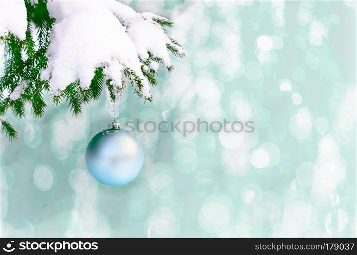 Snow covered fir branch with pale blue Christmas ornament. Christmas greeting background with fir branch and blue ball. Christmas decoration with bauble hanging. Copy space.