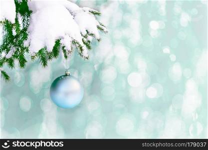 Snow covered fir branch with pale blue Christmas ornament. Christmas greeting background with fir branch and blue ball. Christmas decoration with bauble hanging. Copy space.