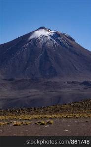 Snow-covered mountain of volcano looms over barren vegetation