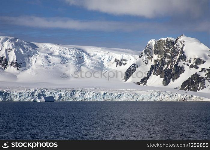 Snow covered mountain range with blue sky and sea in Antarctica