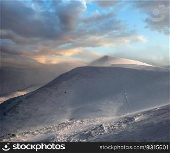 Snow covered mountain slope in last evening sunlight. Magnificent windy dusk on picturesque alpine ski resort, Dragobrat, Ukraine, Carpathian Mountains.