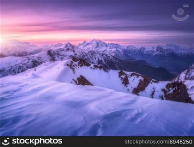 Snow covered mountains and colorful purple sky with clouds at sunset in winter. Beautiful wintry landscape with snowy rocks and hills at twilight. Scenery with alps at frosty evening. Alpine mountains
