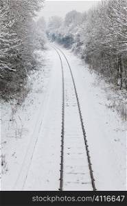 Snow covered railway tracks curving away around a corner into the distance