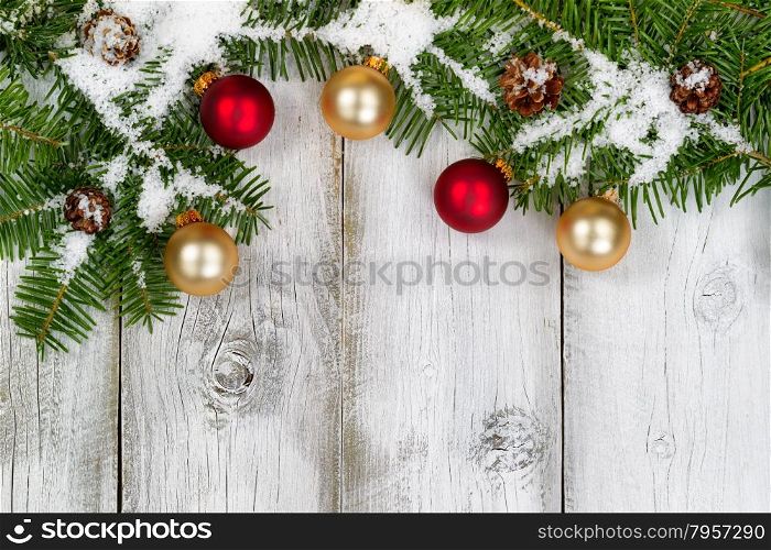 Snow covered real Fir tree branches, ornaments, and cones on rustic white wooden boards. Christmas season concept with top view format.