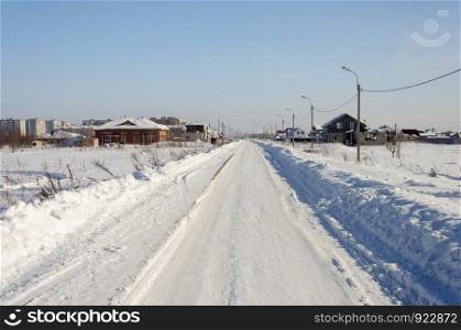 Snow covered road in town, middle lane of Russia. Sunny winter day.