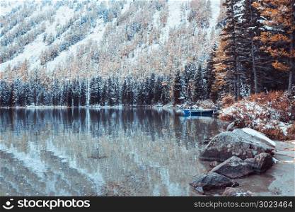 Snow covered shore of a mountain lake. View of the rocks and pine forest in late autumn.