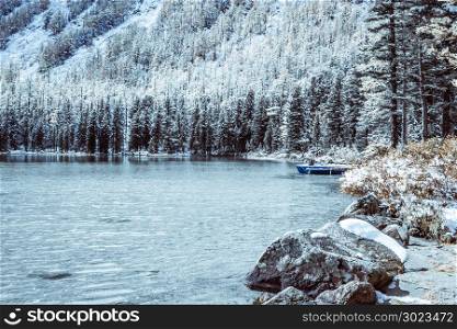 Snow covered shore of a mountain lake. View of the rocks and pine forest in late autumn.