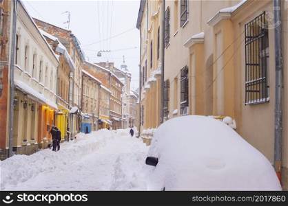 Snow covered street of Lviv old town with cafes and restaurants, car in a huge snowdrift, winter Lviv, Ukraine