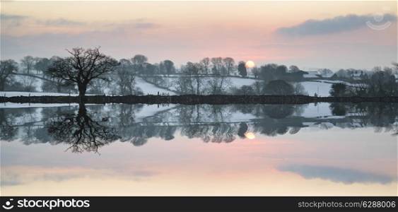 Snow covered Winter countryside sunrise landscape reflected in calm lake