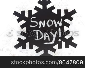 Snow Day! written in chalk on black chalkboard snowflake placed on swirl of silver, wintry ribbons.
