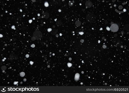 Snow falling on dark winter night. Abstract snowflakes background blur.